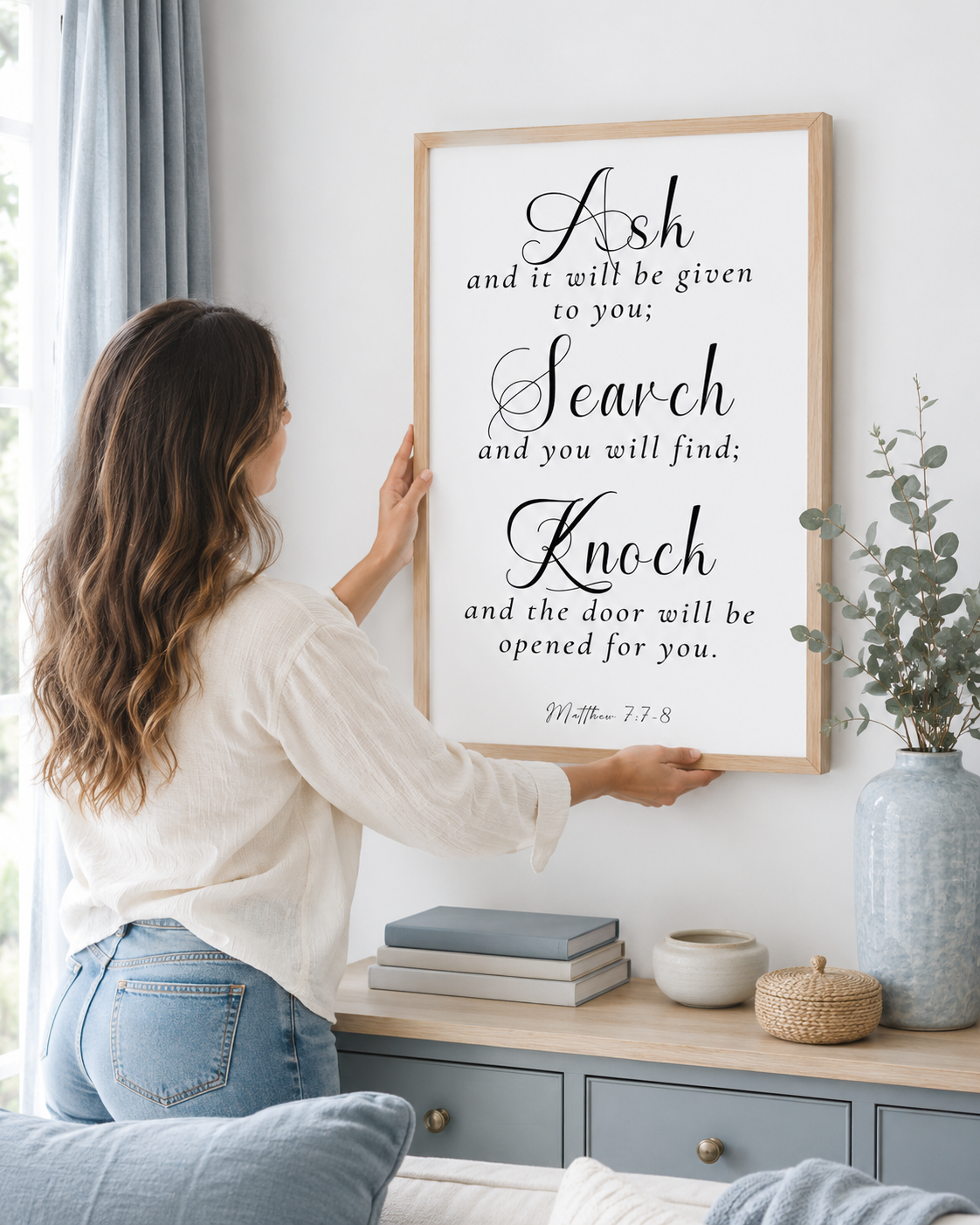 Woman hanging a framed Matthew 7:7-8 print on a wall