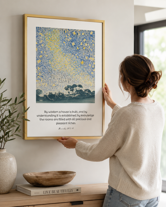 Woman hanging a framed Proverbs 24:3-4 "By Wisdom a House Is Built" print on a wall