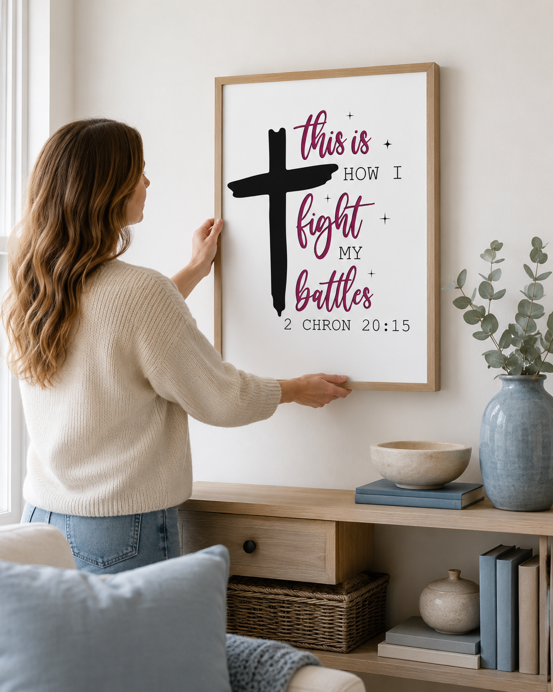 Woman hanging a framed 2 Chronicles 20:15 print on a wall