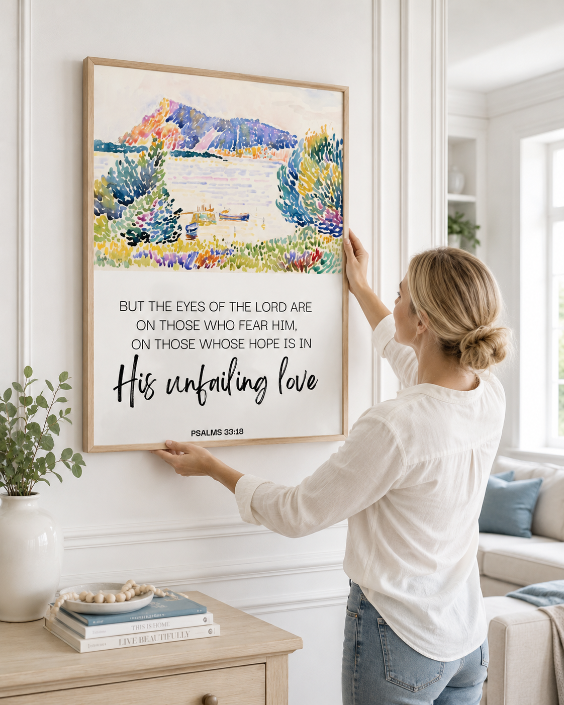 Woman placing framed Psalm 33:18 Christian wall art above a wooden sideboard