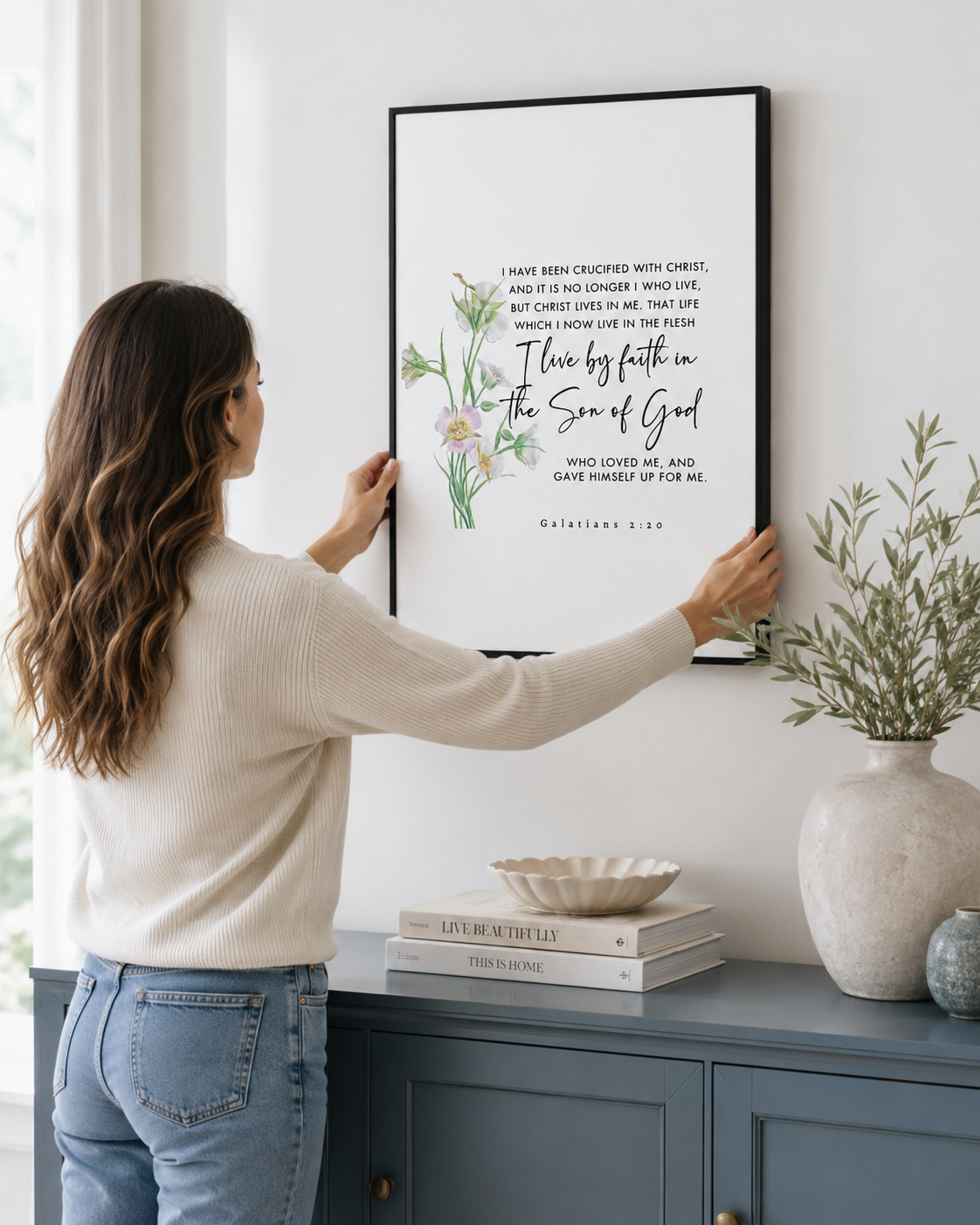 Woman hanging a framed Galatians 2:20 print on a wall