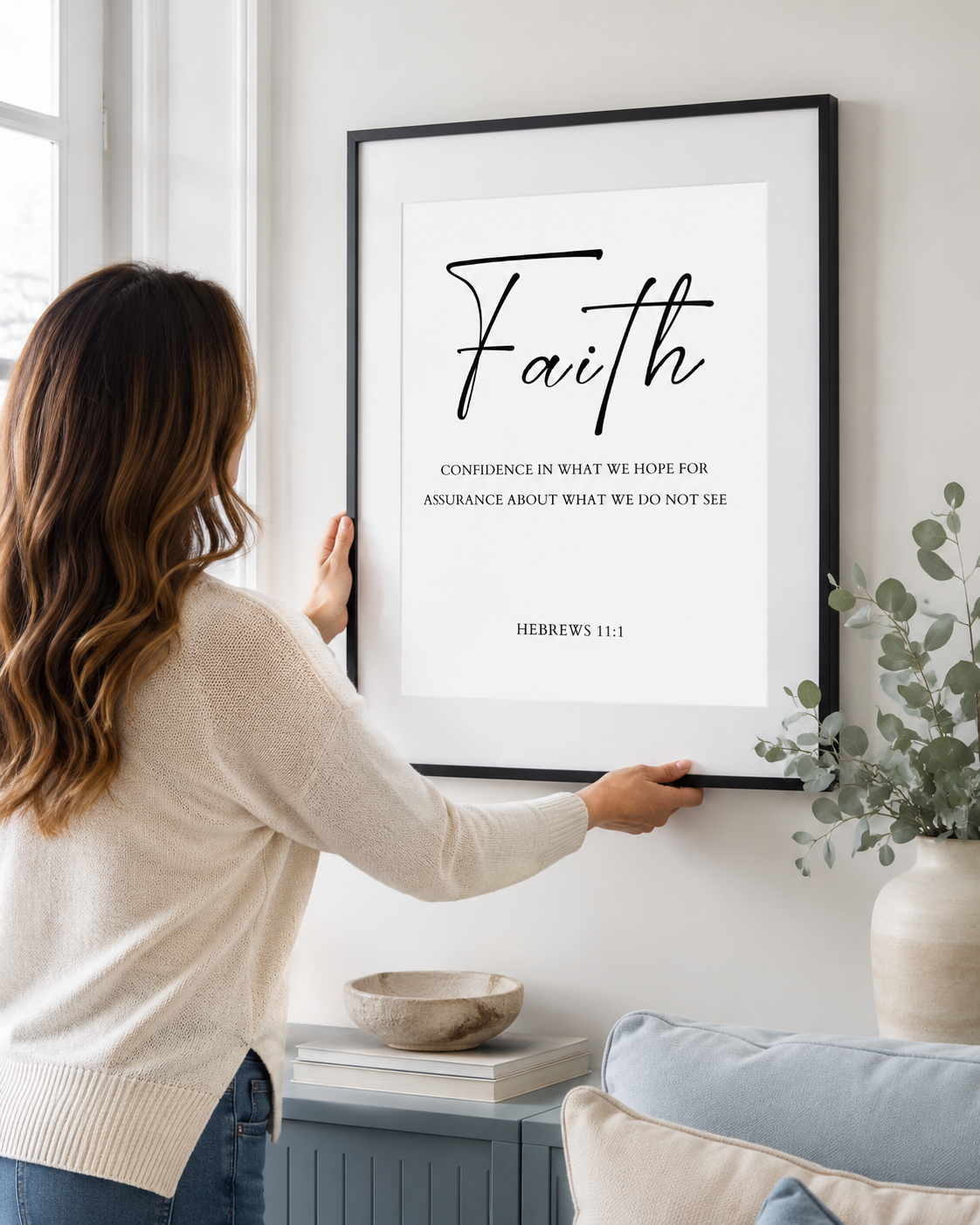Woman hanging a framed Hebrews 11:1 print on a wall