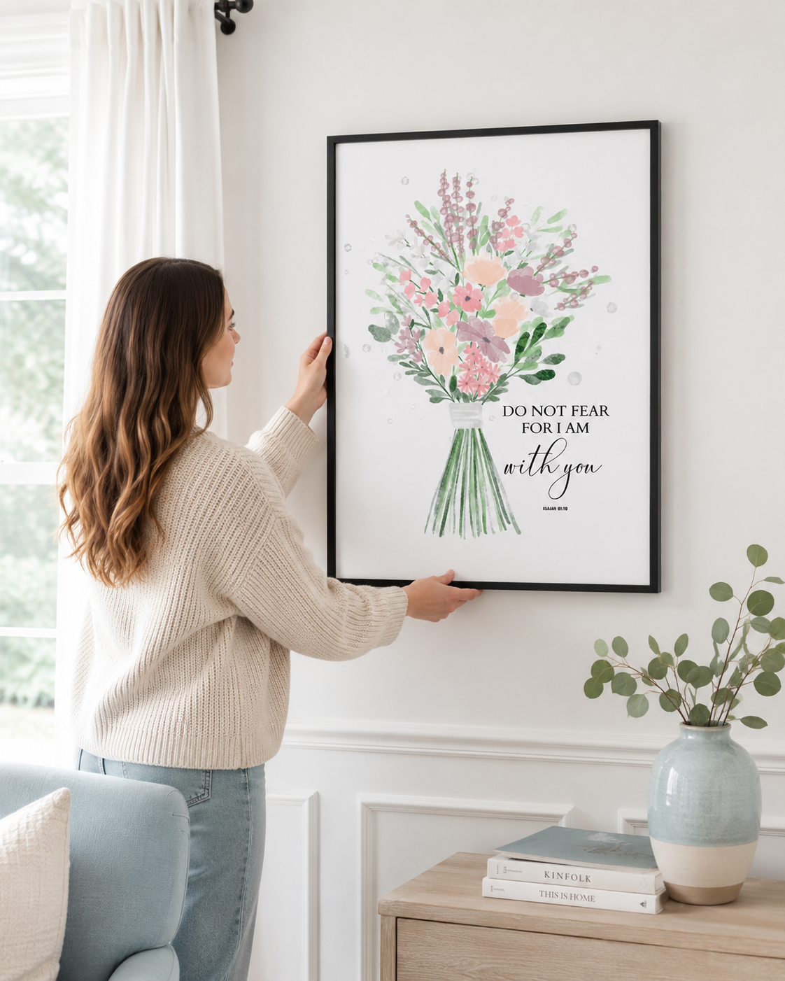 Woman hanging a framed Isaiah 41:10 print on a wall