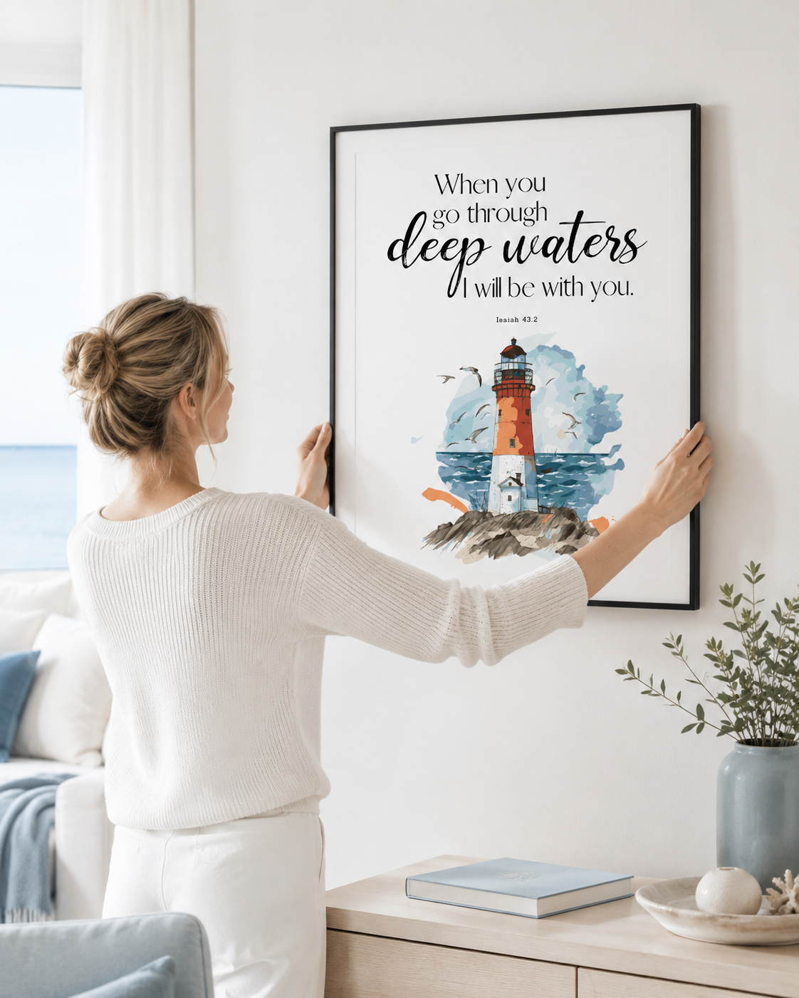 Woman hanging a framed Isaiah 43:2 lighthouse print on a wall