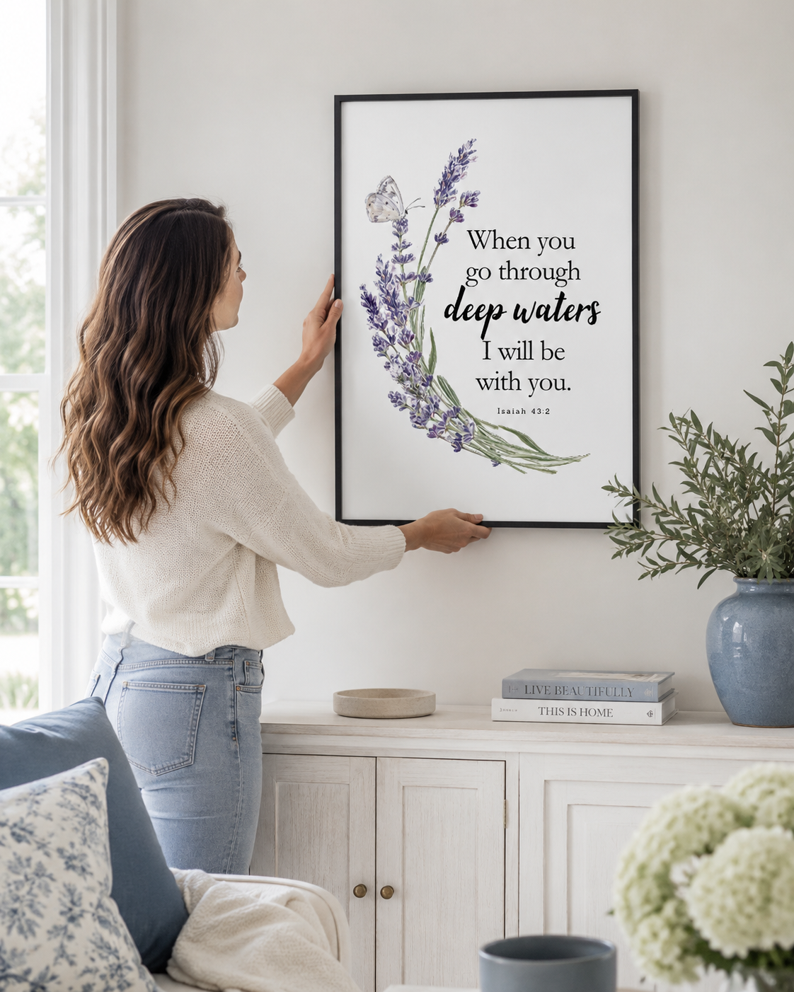 Woman hanging a framed Isaiah 43:2 print on a wall