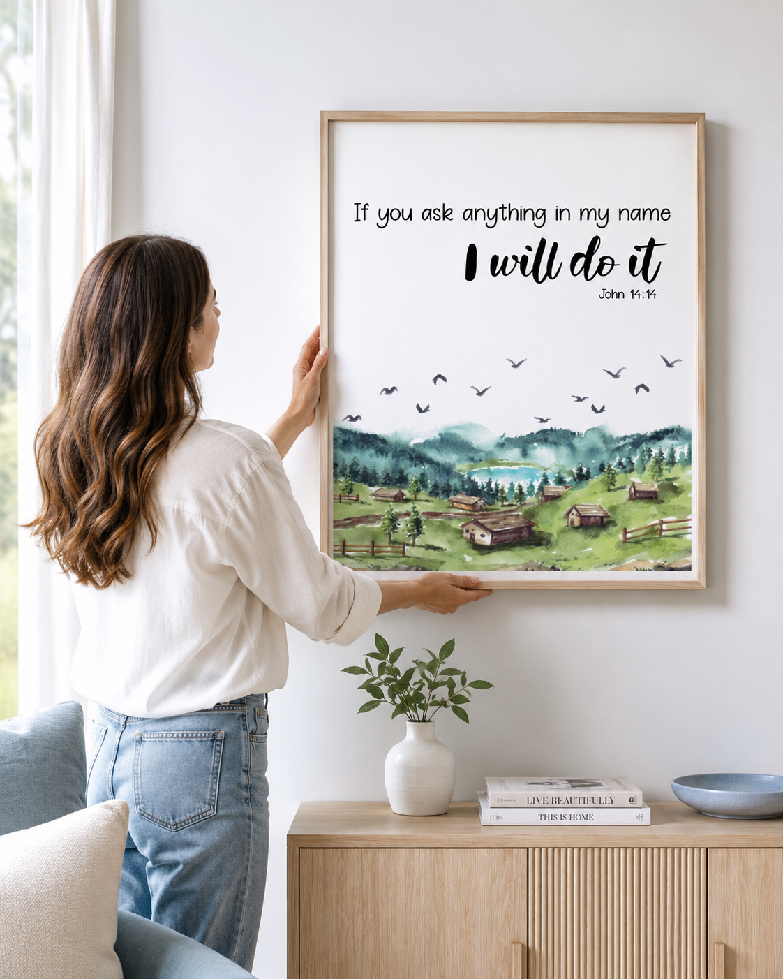Woman hanging a framed John 14:14 "ask in my name" print on a wall