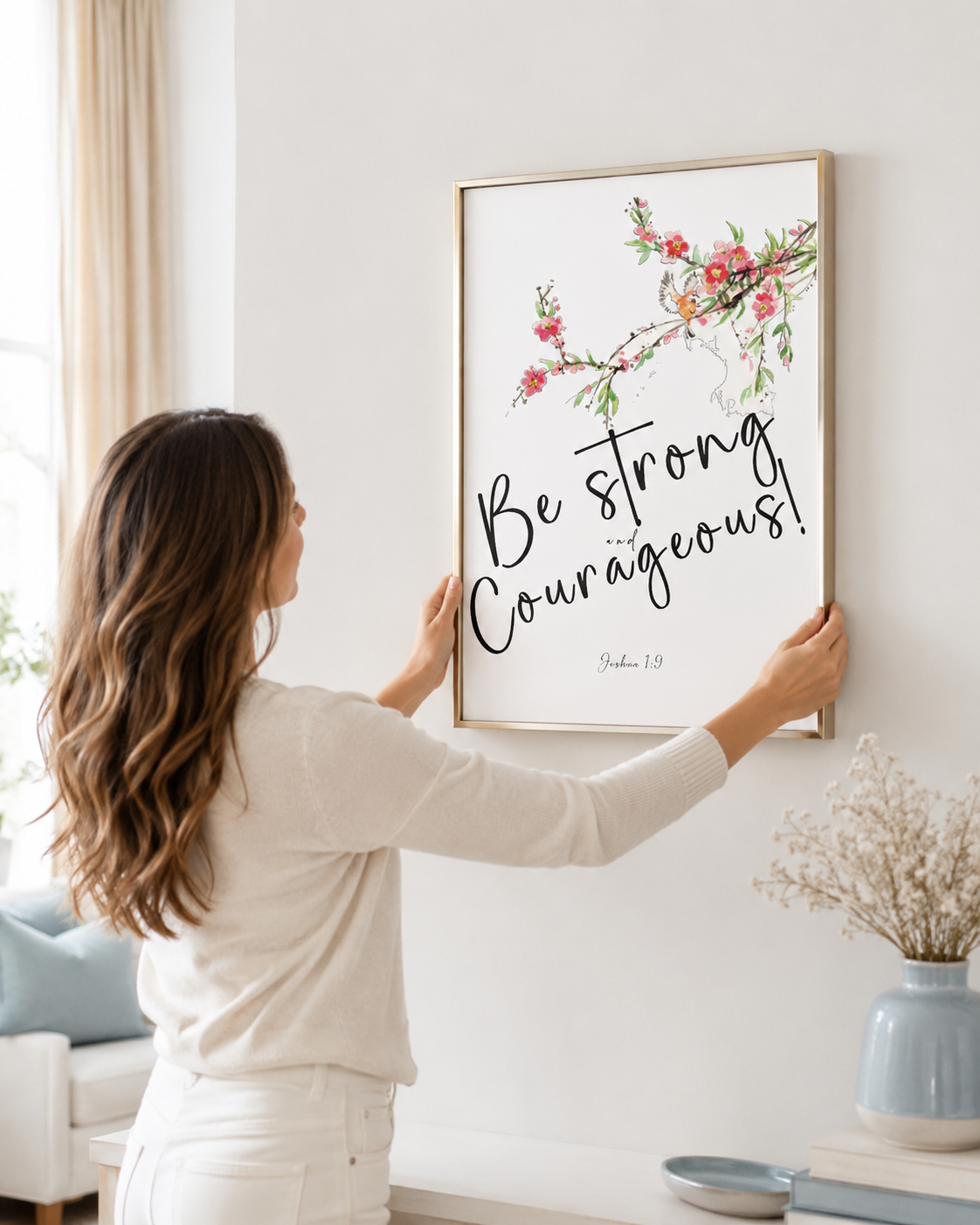 Woman hanging a framed Joshua 1:9 floral print on a wall