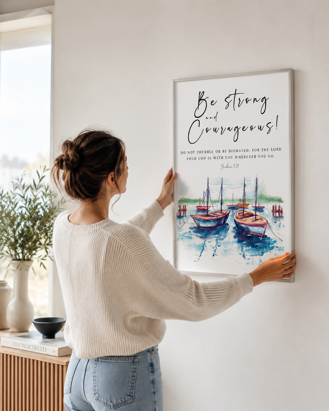 Woman hanging a framed Joshua 1:9 nautical print on a wall