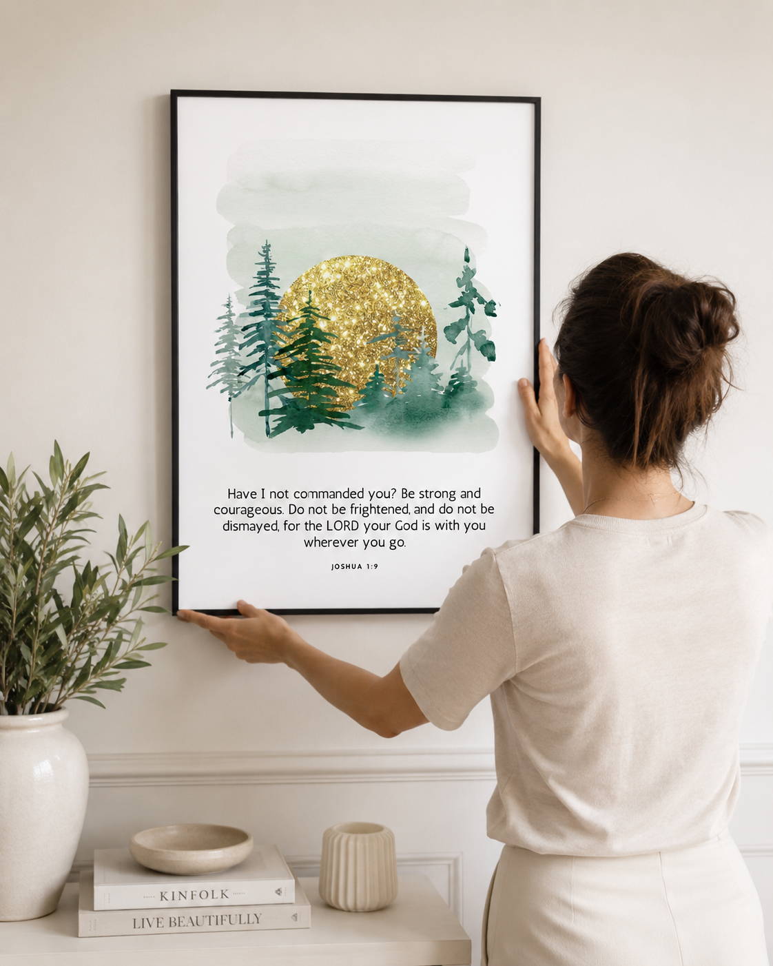 Woman hanging a framed Joshua 1:9 print on a wall