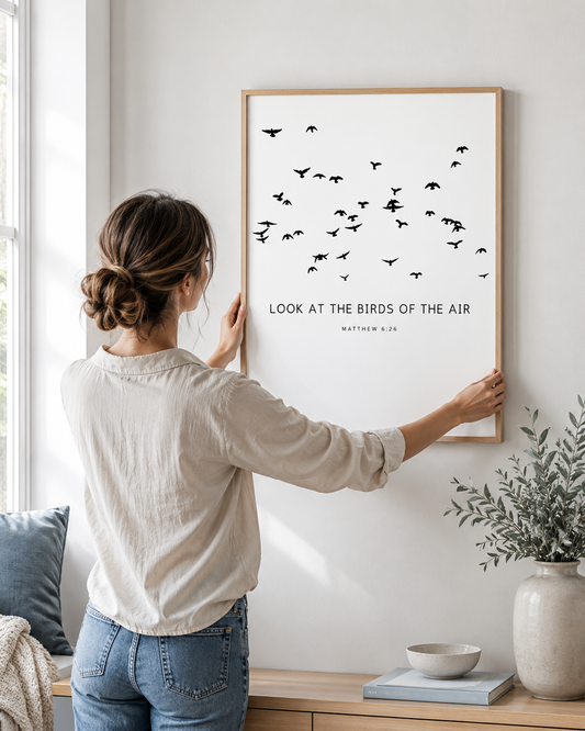 Woman hanging a framed Matthew 6:26 print on a wall