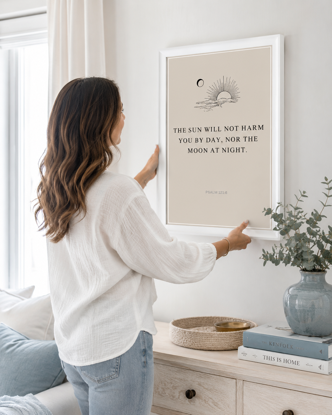 Woman hanging a framed Psalm 121:6 print on a wall