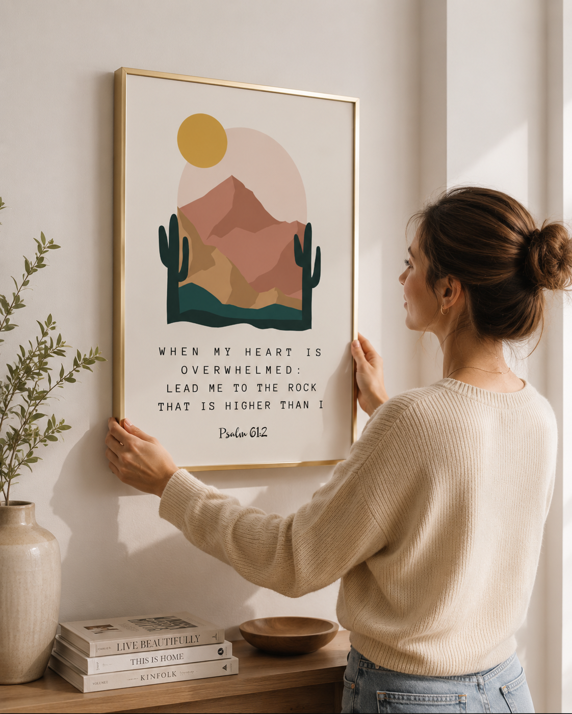 Woman hanging a framed Psalm 61:2 "lead me to the rock" print on a wall