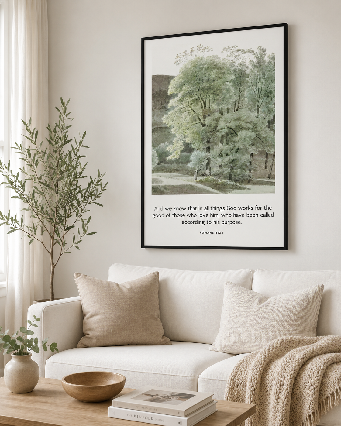 Black-framed Romans 8:28 wall art print displayed above a neutral linen sofa in a modern living room